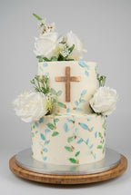 gâteau baptême  deux etages avec dessin a la main de brindille de fleurs ,une croix chrétienne au milieu et des rose blanche autour et dessus 