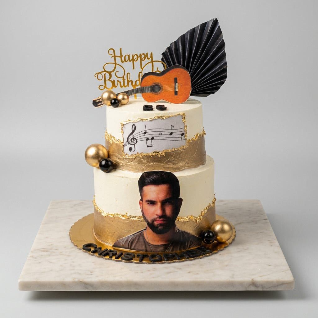 gâteau deux étages kendji girac , doré et couleur vanille , il  la photo du chanteur en vas puis a letage a droite deux boule une doré et une noir au milieu des note de musique , au dessus  boule deux doré et une noir , une guitare le chiffre  et écrit en doré happy birthday 